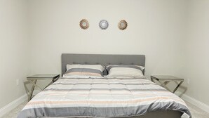 A bedroom with a grey bed, striped bedding, two nightstands, and decorative wall art. - Entire House close to everything. (Seffner)
