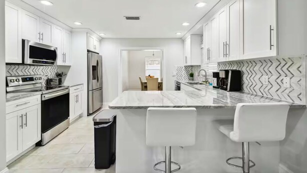 A modern kitchen with white cabinetry, stainless steel appliances, and a marble island with bar stools. - Entire House close to everything. (Seffner)