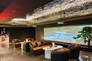 A modern lounge area with sofas, a coffee table, and a large screen displaying a nature scene. - Lijing Peninsula Hotels (Lufeng)