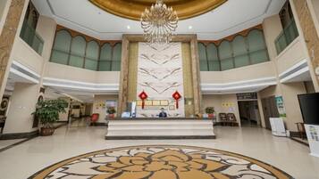 A spacious lobby with a central reception desk, a chandelier, and a large floral patterned floor.
