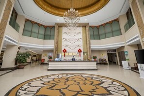 A spacious lobby with a central reception desk, a chandelier, and a large floral patterned floor. - Lijing Peninsula Hotels (Lufeng)