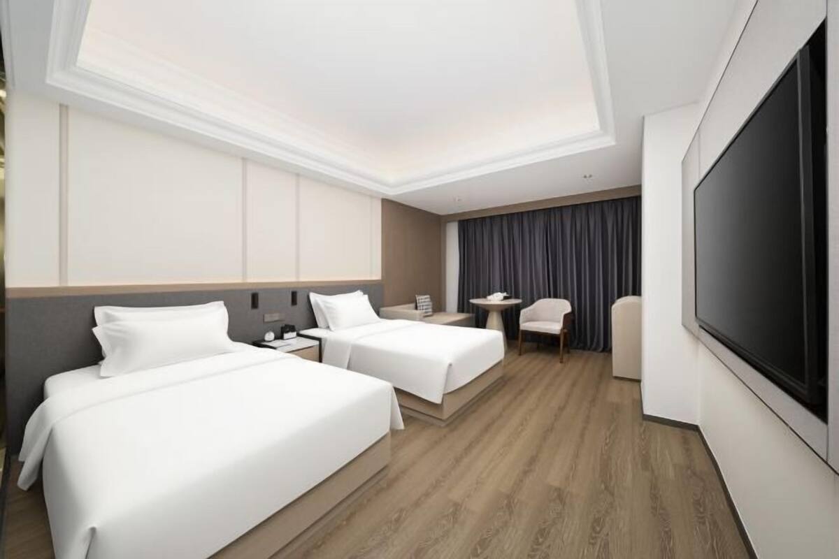 A hotel room with two beds, a desk, a chair, a TV, and a large window.