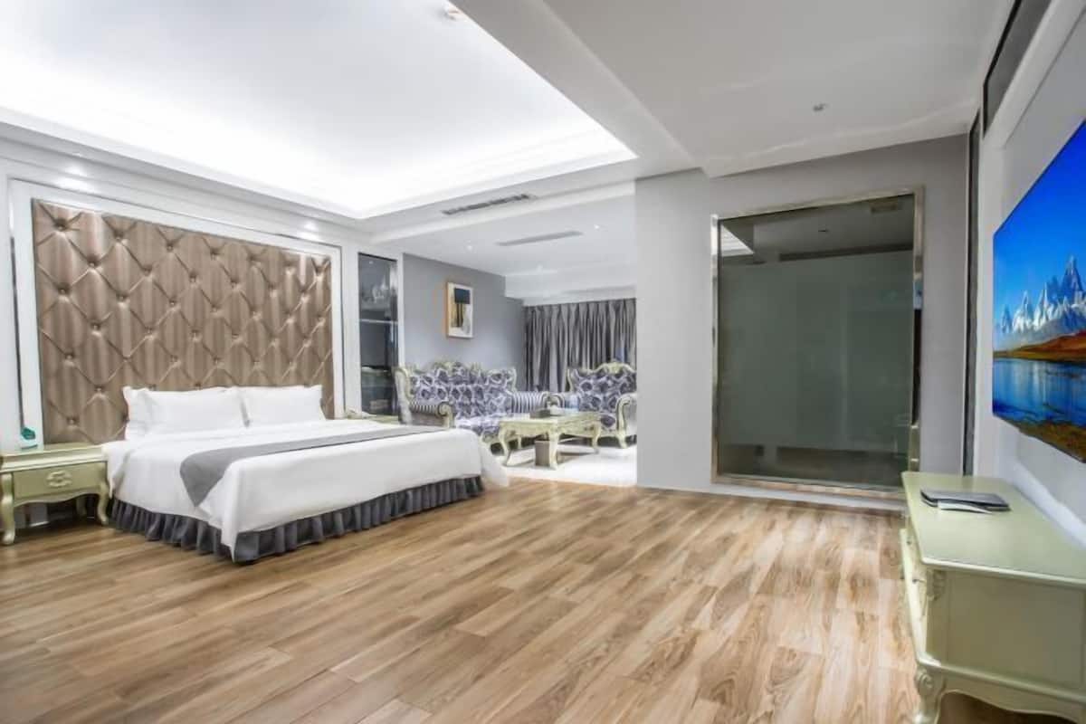 A modern hotel room with a large bed, a seating area with a table, and a large window.