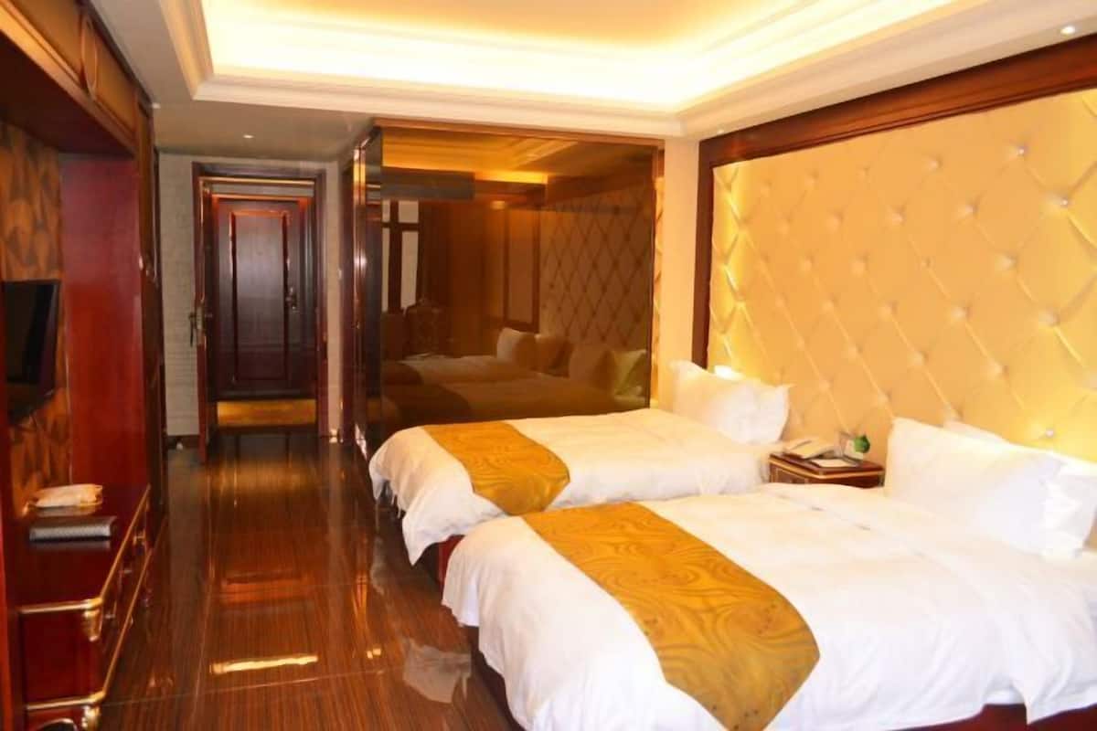 A hotel room with two beds, a wooden floor, a large tufted headboard, and a mirror on the wall.