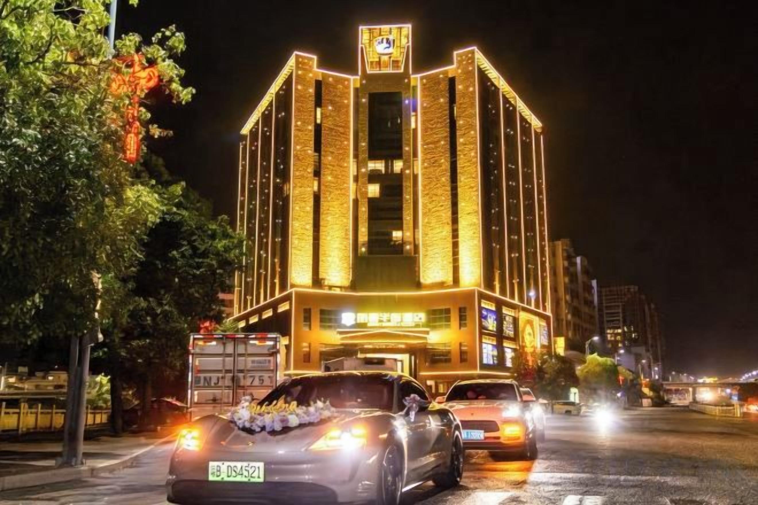 Un edificio bien iluminado con un cartel llamativo en la parte superior, una entrada espaciosa y una calle con vehículos a la vista.