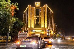 A brightly lit building with a prominent sign at the top, a large entrance, and a visible street with vehicles. - Lijing Peninsula Hotels (Lufeng)