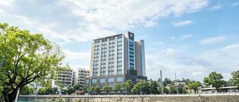 A modern hotel with a view of a river, surrounded by greenery and other buildings.