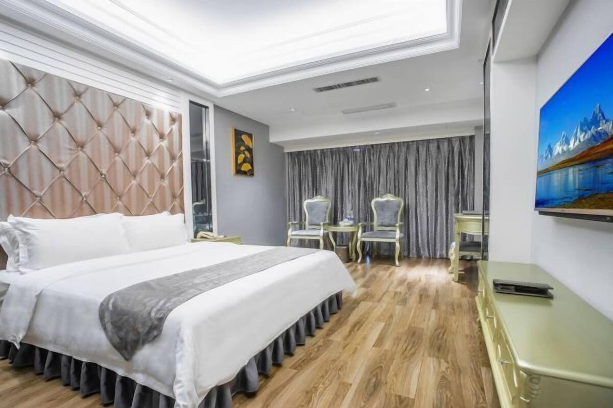A hotel room with a large bed, a TV on the wall, and a painting of mountains.