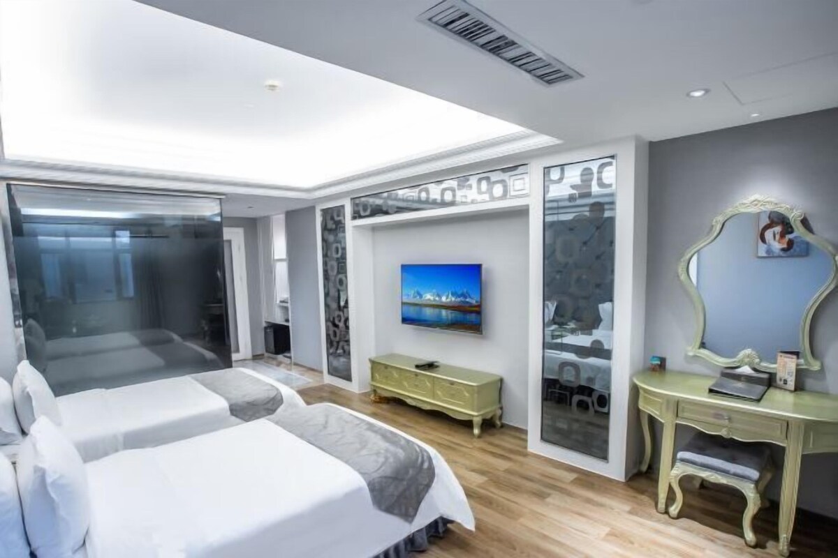 Un dormitorio moderno con una cama grande, televisor, tocador y cabina de ducha de vidrio.