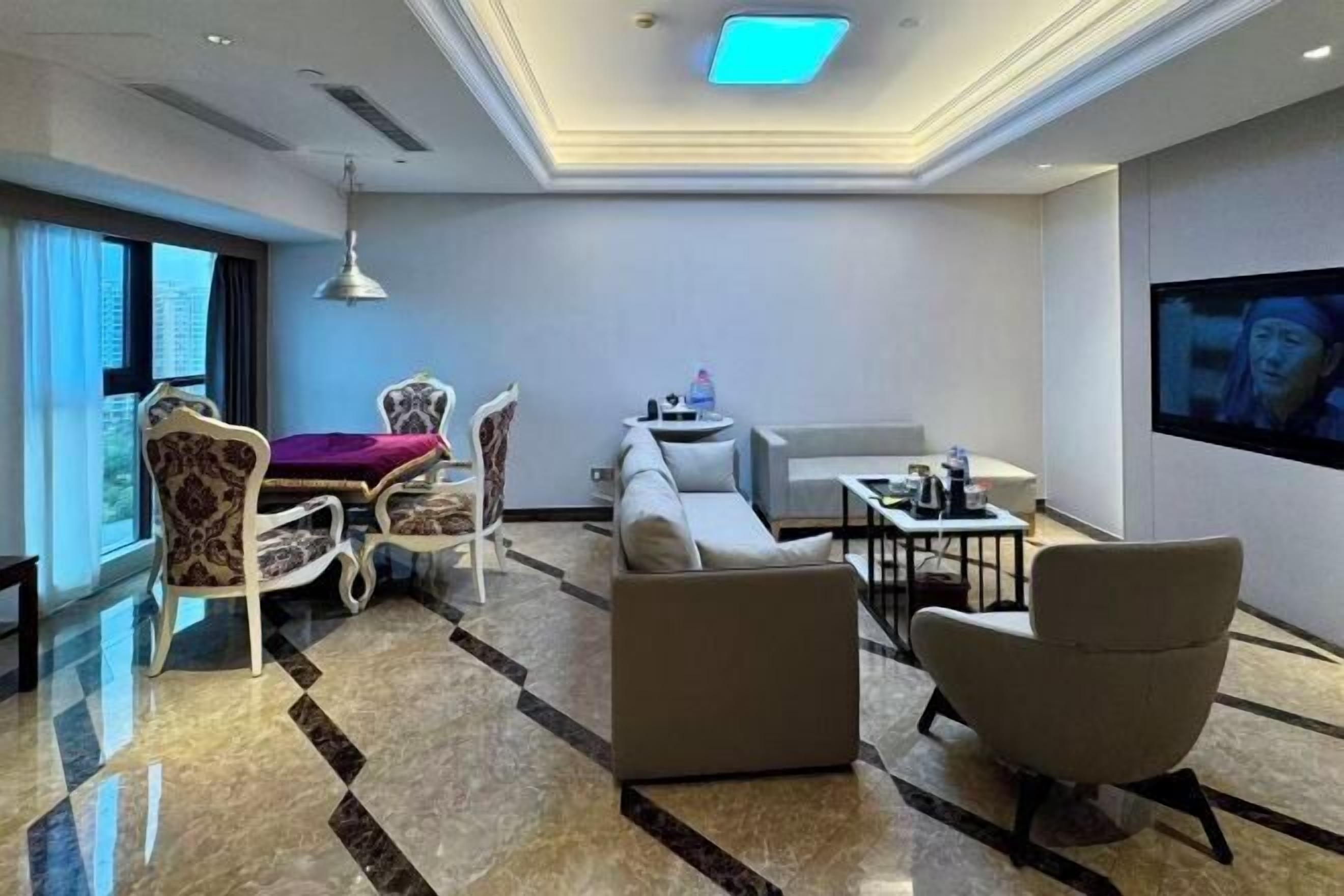 Una habitación de hotel moderna con sofá, sillones, mesa de comedor y televisor.