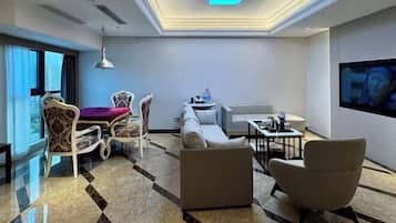 Una habitación de hotel moderna con sofá, sillones, mesa de comedor y televisor.