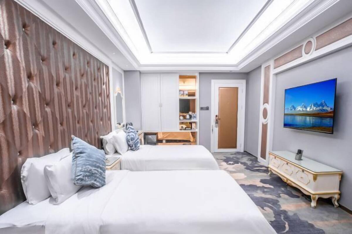 A hotel room with two beds, a wooden headboard, a television, and a wardrobe.