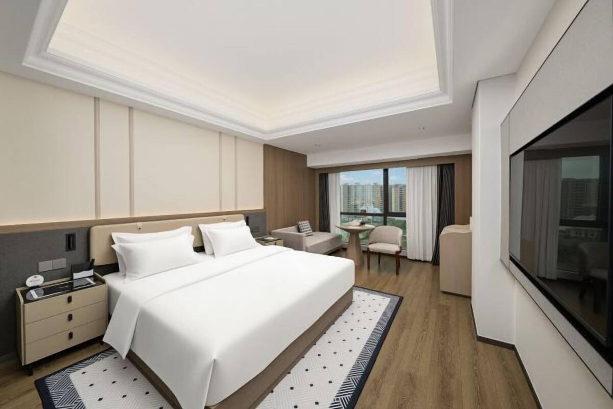 A modern hotel room with a large bed, a desk, a chair, and a view of the city.