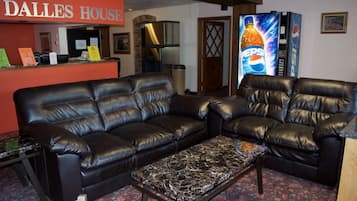 A living room with two black leather sofas, a marble coffee table, and a red sign reading "DALLES HOUSE".
