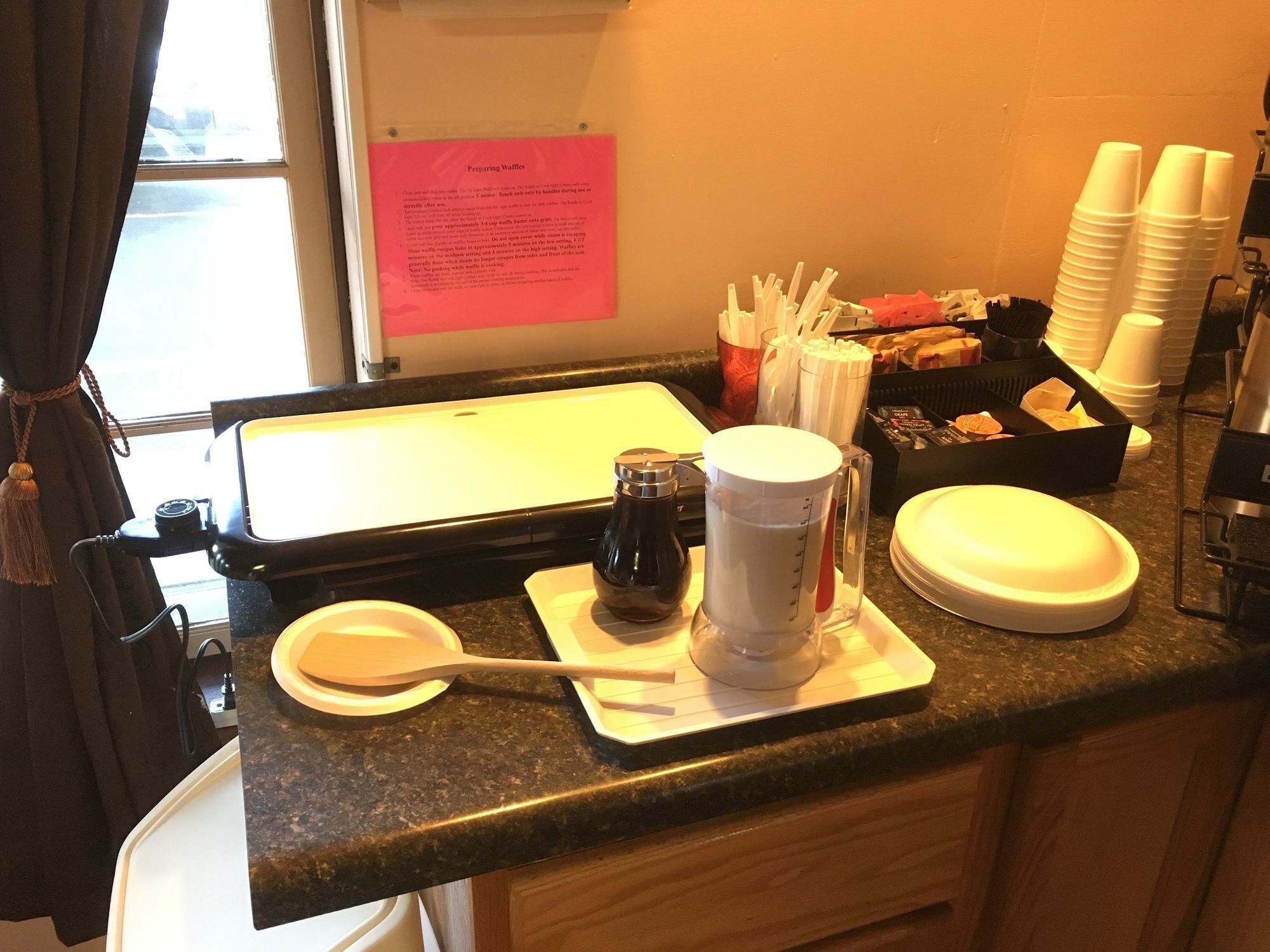 A kitchen counter with a waffle maker, a coffee pot, and a waffle recipe card.
