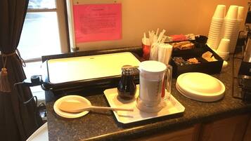 A kitchen counter with a waffle maker, a coffee pot, and a waffle recipe card.