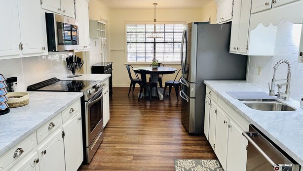 Una cucina moderna con mobili bianchi, elettrodomestici in acciaio inossidabile e un'area pranzo con tavolo e sedie.