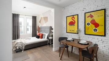 A modern bedroom with a bed, a dining table with chairs, and two framed posters on the wall.