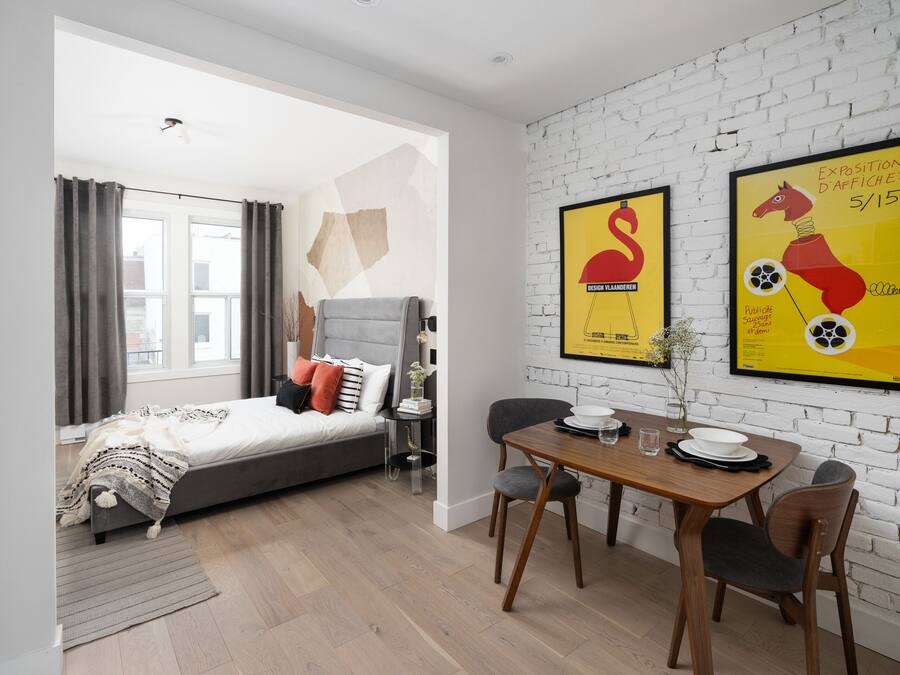 A modern bedroom with a bed, a dining table with chairs, and two framed posters on the wall.