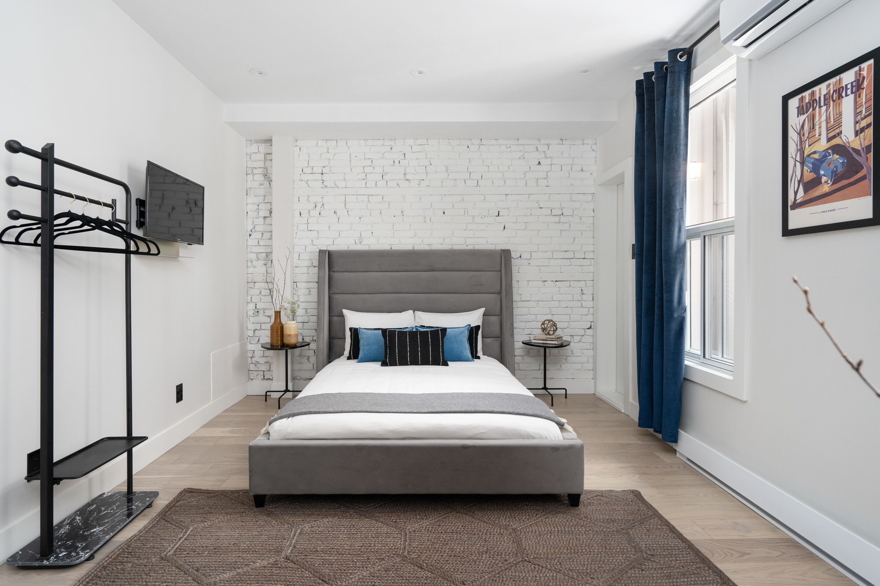 Ein modernes Schlafzimmer mit grauem Bett, weißer Ziegelwand und blauem Vorhang.