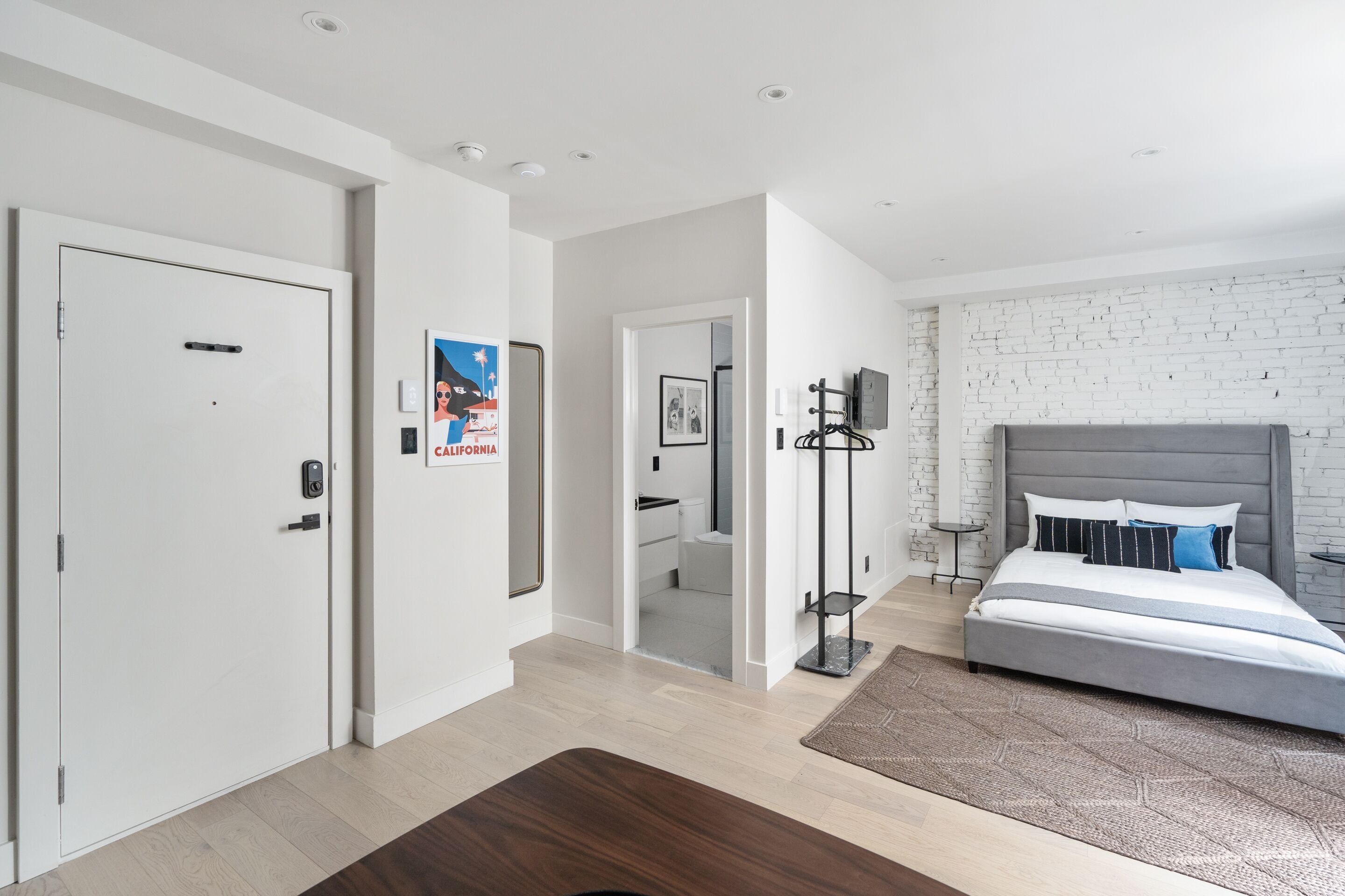 Une chambre moderne avec un lit, un plancher en bois, un mur en briques blanches et une porte.