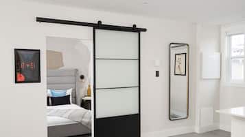 Una camera da letto moderna con porta scorrevole, un letto con biancheria da letto bianca, un comodino con lampada e un grande specchio a parete.