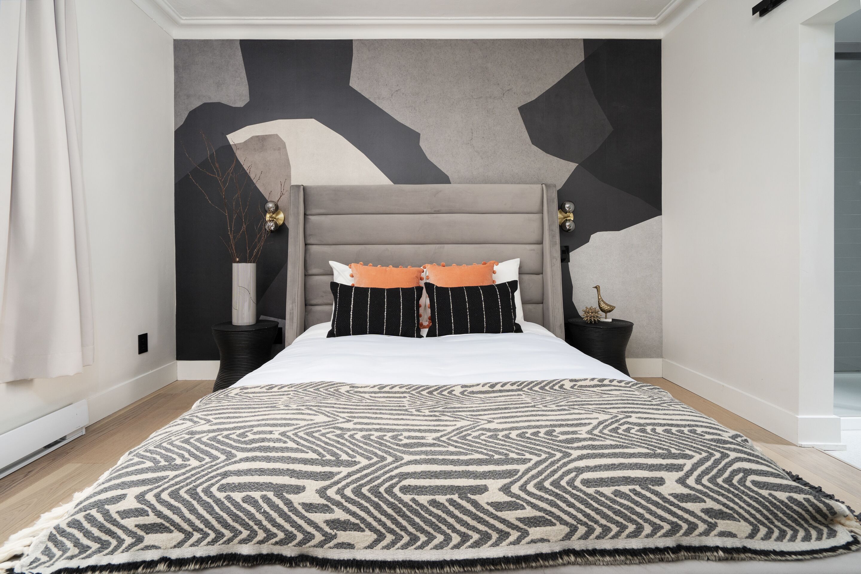 A modern bedroom with a large bed, a geometric-patterned rug, and a unique wall design.