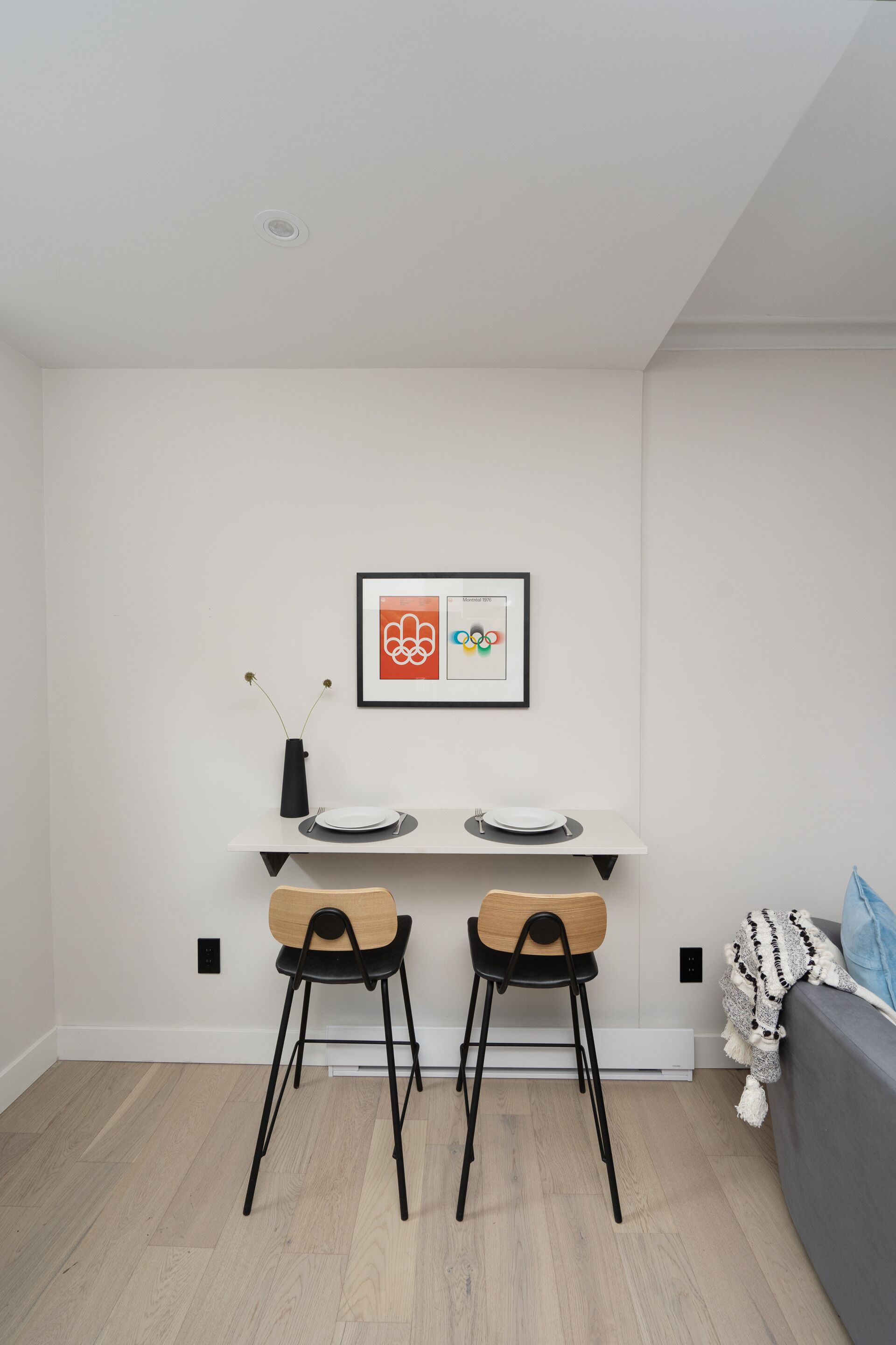 Eine moderne Küche mit weißer Arbeitsplatte, zwei Barhocker, einem gerahmten Bild und einem grauen Sofa.