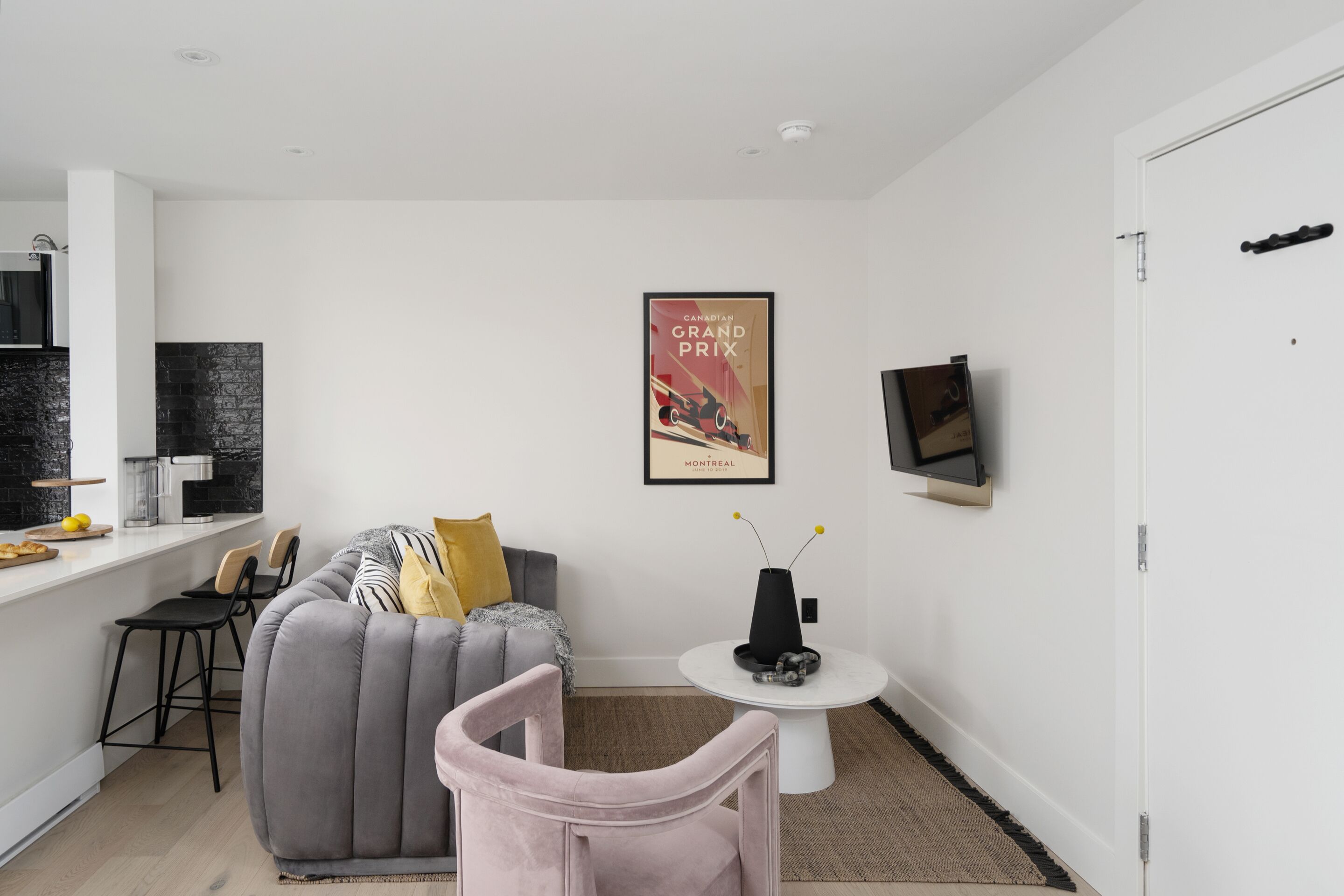 A modern living room with a grey sofa, a small round table, and a TV mounted on the wall.