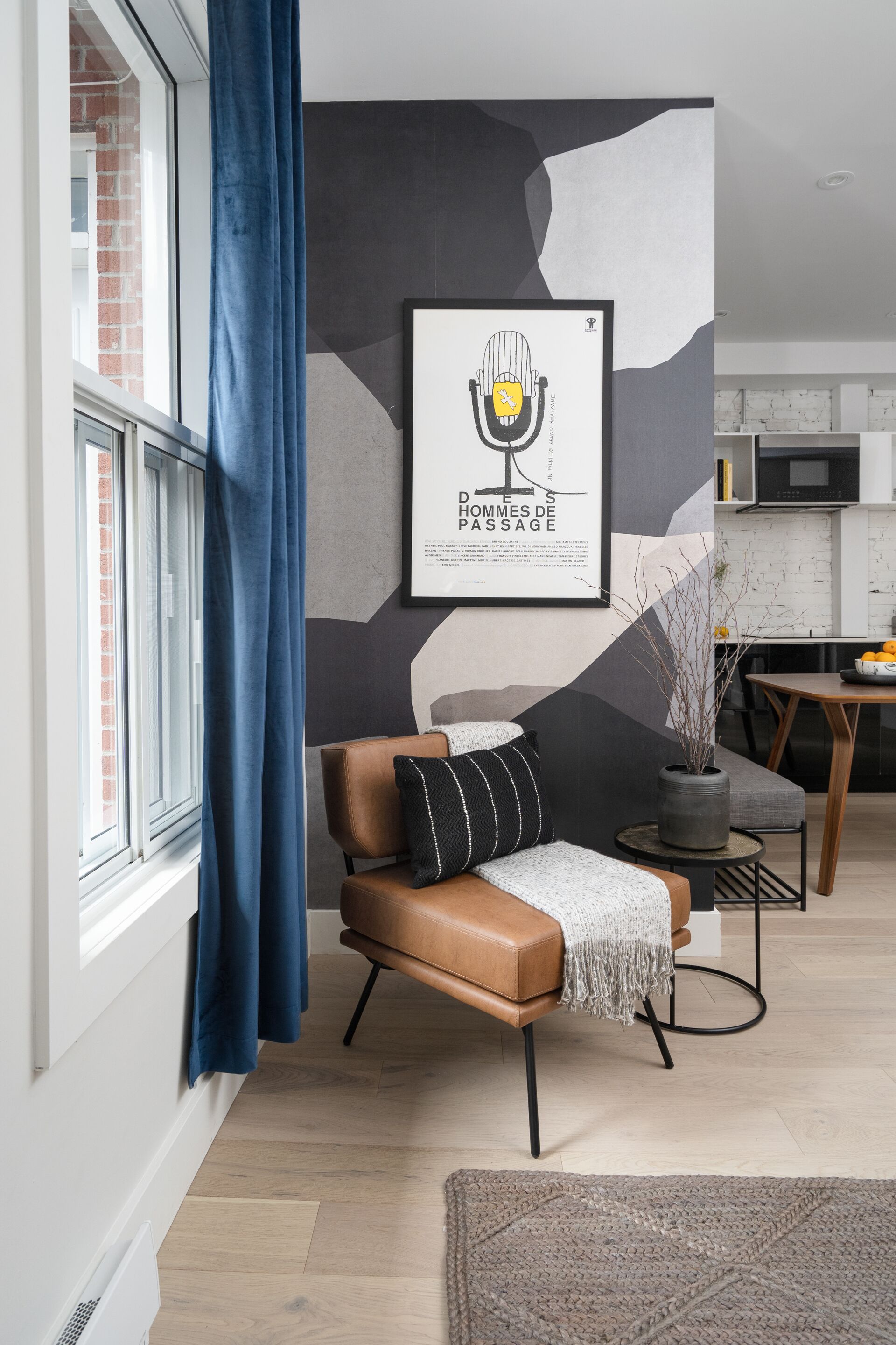 A modern living room with a leather sofa, a framed artwork on the wall, and a view of the kitchen in the background.