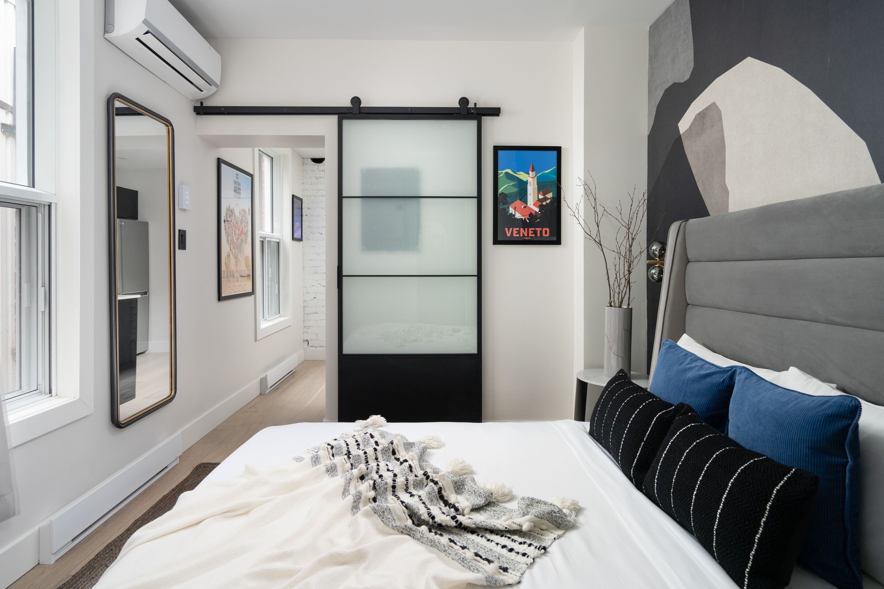 A modern bedroom with a bed, a sliding glass door, a large abstract painting, and a framed picture of Venice.