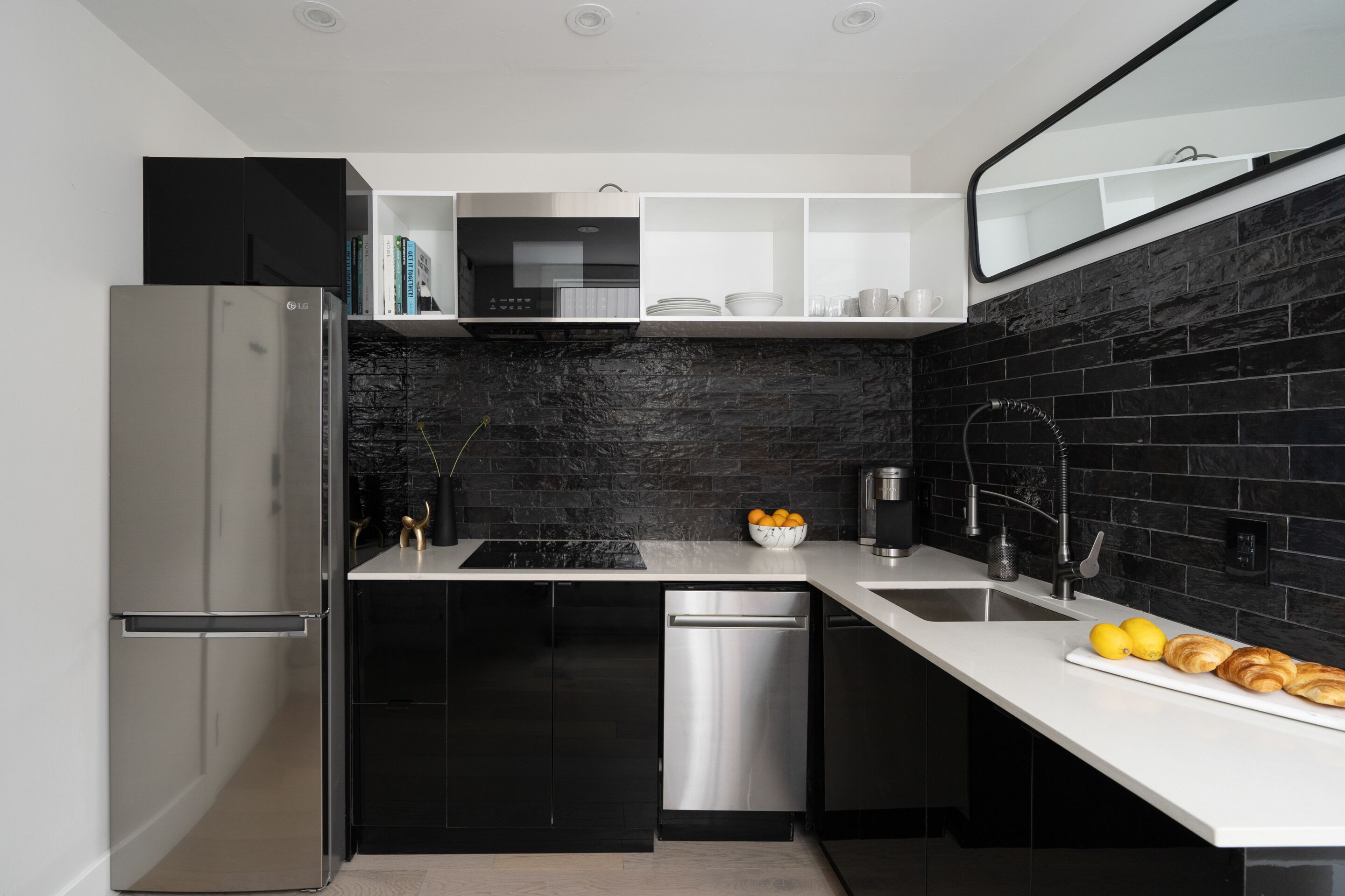 A modern kitchen with black cabinetry, a stainless steel refrigerator, a dishwasher, and a black tiled backsplash.