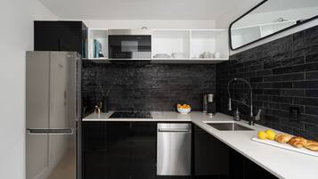A modern kitchen with black cabinetry, a stainless steel refrigerator, a dishwasher, and a black tiled backsplash.