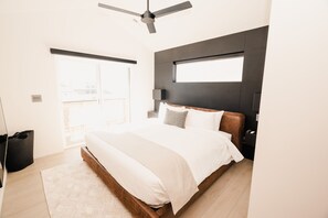 A modern bedroom with a large bed, a ceiling fan, a window, and a view of the city. - NEW- Modern Home Close to Downtown - Hot Tub! (Bozeman)