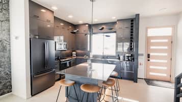 Une cuisine moderne dotée d’un grand îlot central, de tabourets de bar, d’appareils électroménagers en acier inoxydable et d’un design minimaliste.