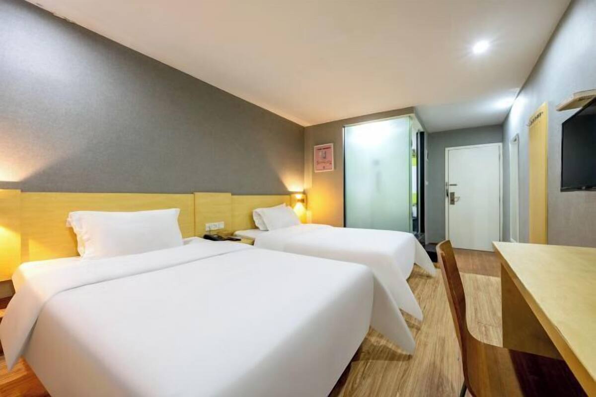 A hotel room with two beds, a wooden desk, and a small table.