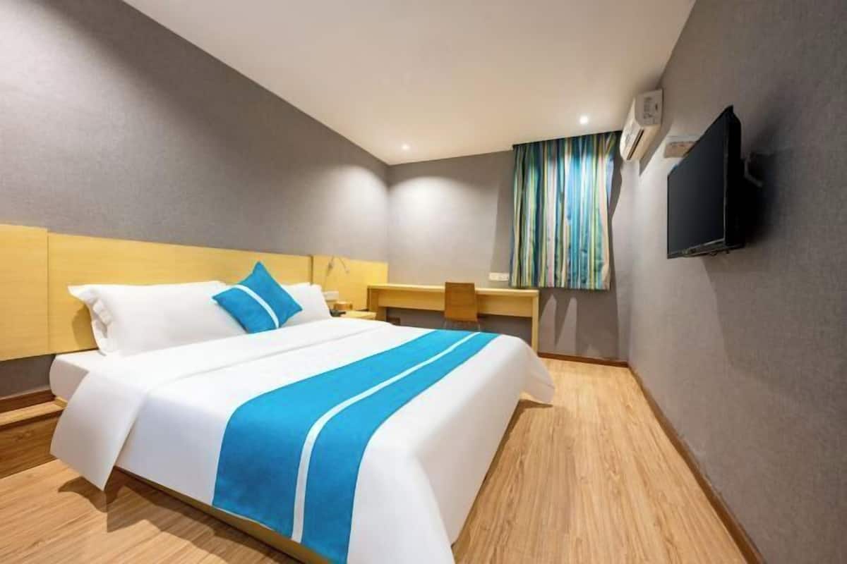A hotel room with a bed, a desk, a chair, a TV, and a window with curtains.