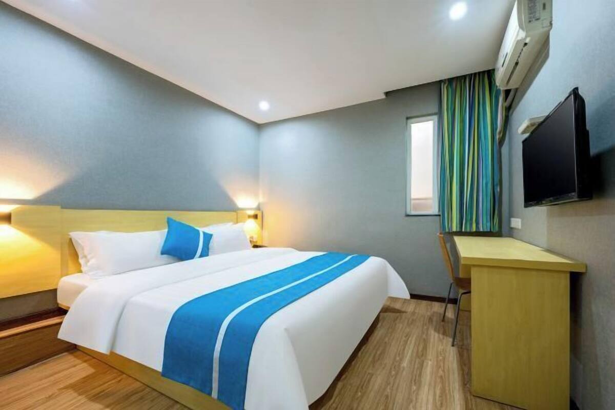 A hotel room with a bed, bedside table, desk, and a television.