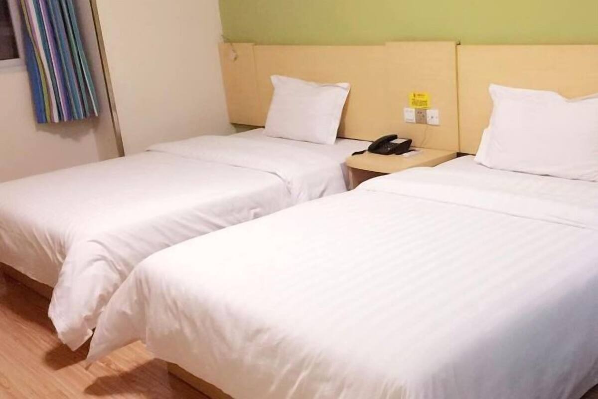 A hotel room with two single beds, a bedside table with a phone, and a window with curtains.
