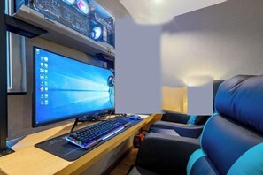 A modern gaming setup with a monitor, keyboard, and mouse on a wooden desk, with a gaming chair and a wall-mounted computer tower. - Xiyue Hotel (Dongguan Chang'an Vanke Plaza Branch) (Dongguan)