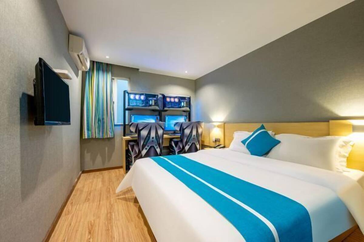 A hotel room with a large bed, a desk with two monitors, and a television on the wall.