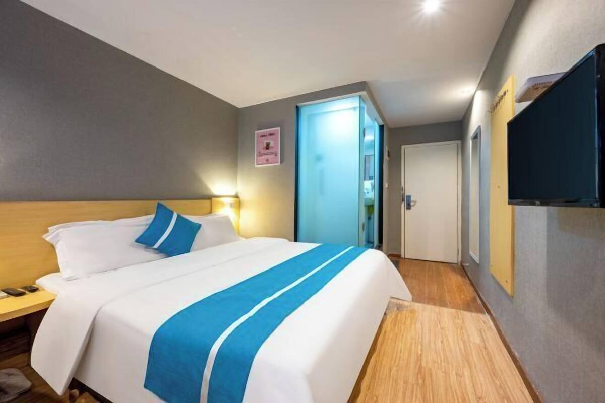 A hotel room with a bed, bedside table, and a door leading to another room.