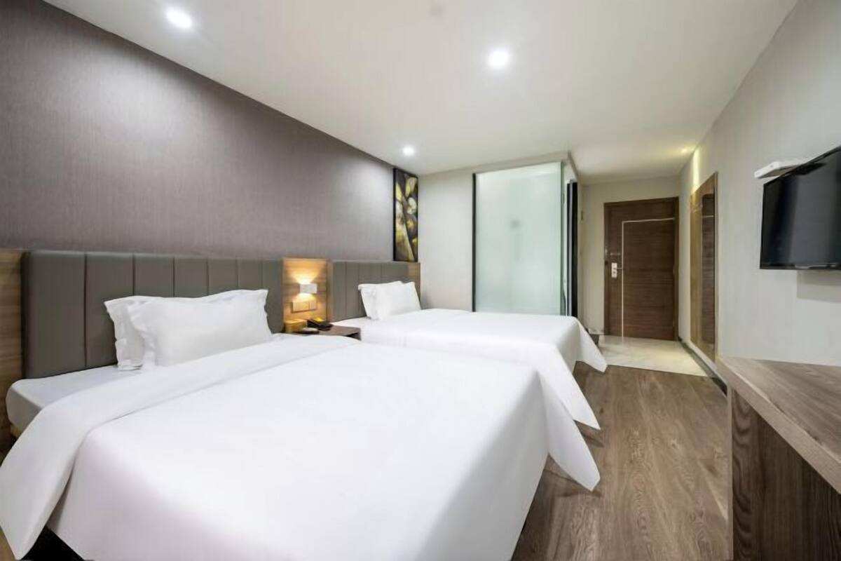 A hotel room with two beds, a TV, and a wooden floor.