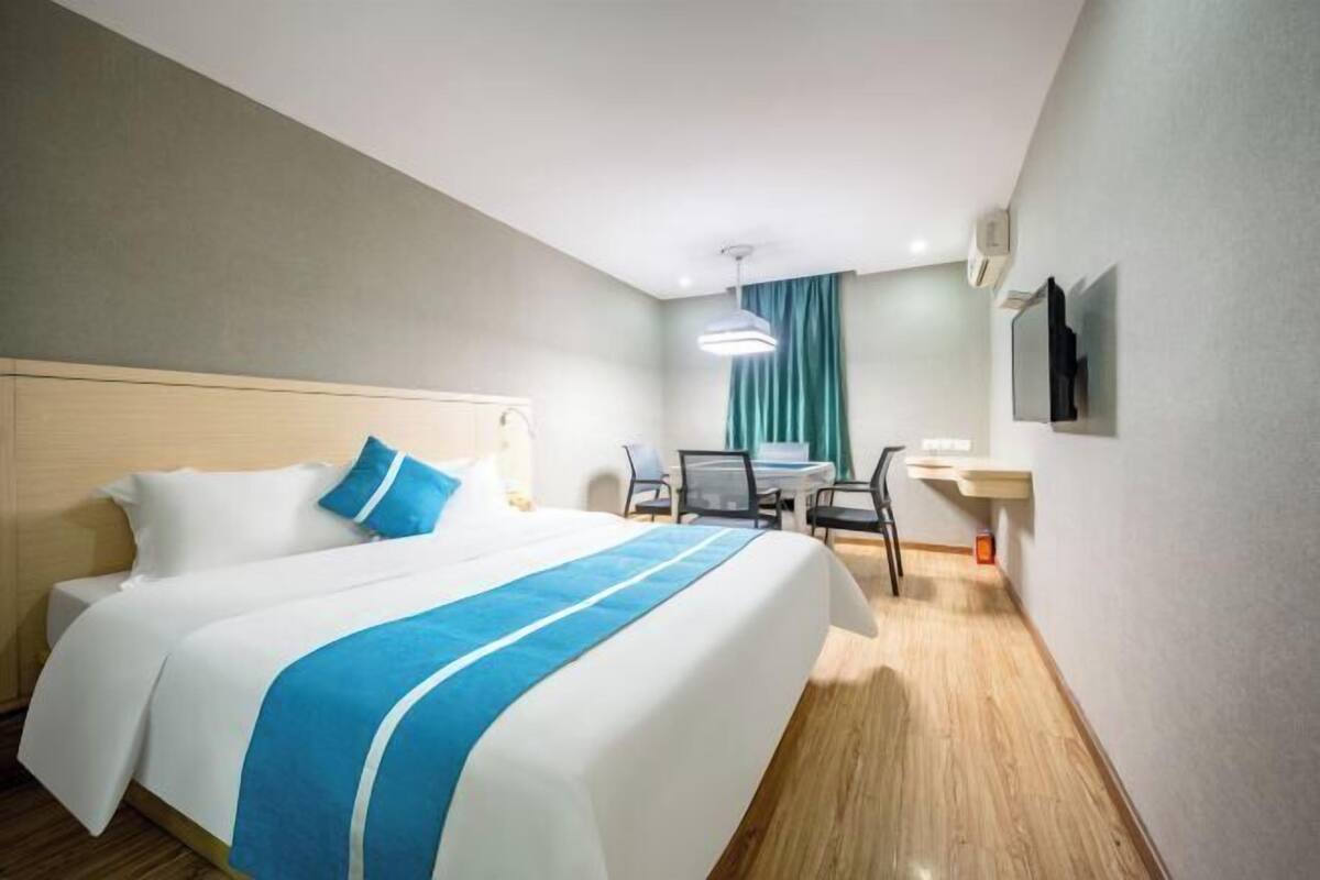 A hotel room with a bed, a desk, a chair, a TV, and a window with curtains.