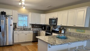 A modern kitchen with white cabinets, stainless steel appliances, a granite countertop, and a bar stool area. - 2nd row Ocean Views 4br 3ba Sleeps 12, '26 Pool Amenity Card, linens included (Edisto Island)