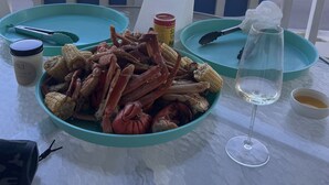 A table with a bowl of seafood, a wine glass, and a candle on a balcony overlooking a house. - 2nd row Ocean Views 4br 3ba Sleeps 12, '26 Pool Amenity Card, linens included (Edisto Island)