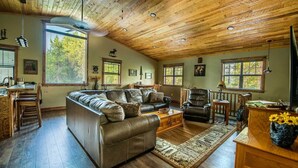 A cozy living room with a wooden ceiling, leather sofas, a coffee table, and a rug.