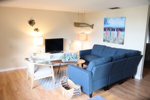 A living room with a blue sofa, a TV, a lamp, and a painting of beach umbrellas. - Noko Life on Shore T (Nokomis)
