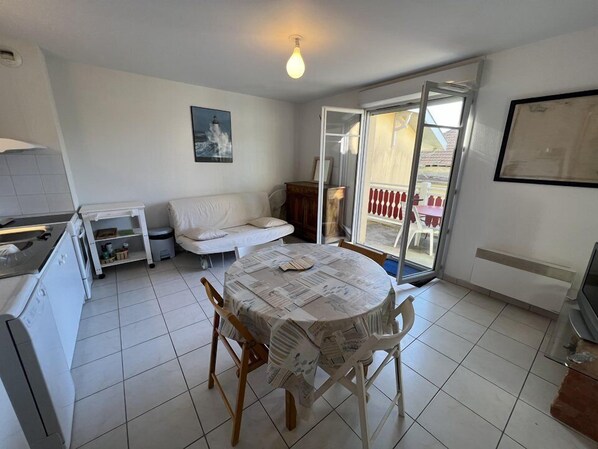 A compact living space with a dining table, a sofa, a kitchen area, and a sliding glass door leading to an outdoor area.