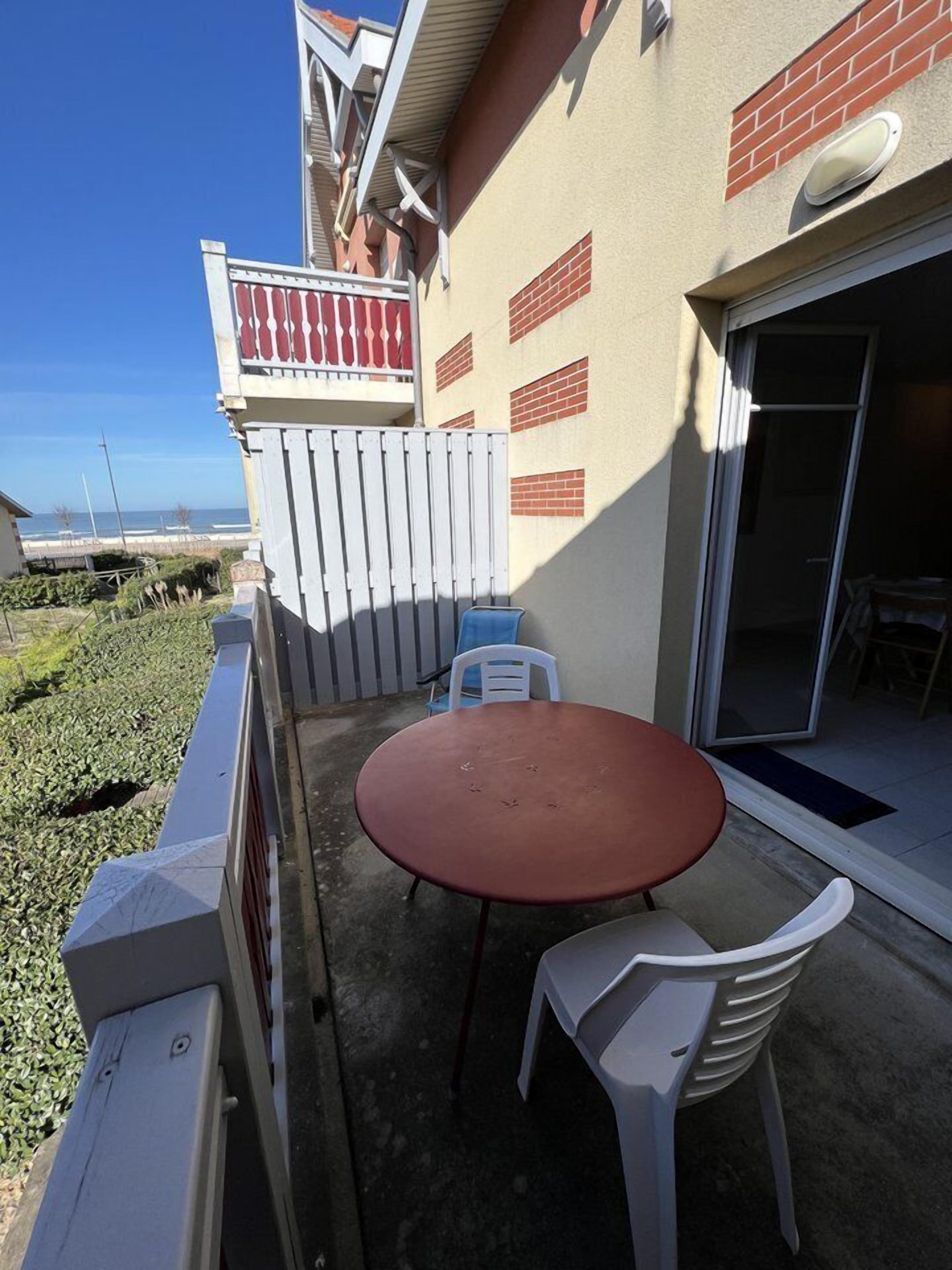 Eine Terrasse mit einem runden Tisch und zwei Stühlen, einem weißen Zaun und Blick auf den Ozean.